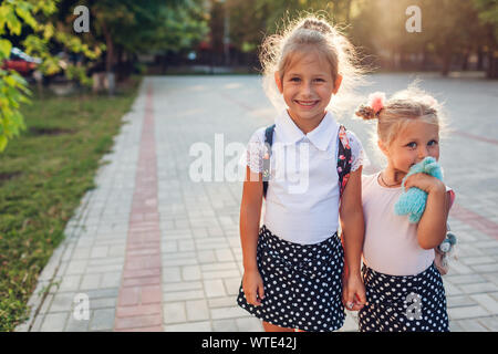 Glückliche Schwestern Mädchen, Rucksäcke und halten sich an den Händen. Kinder, Schüler, Aufenthalt im Freien Grundschule nach Klassen. Bildung. Zurück zur Schule Stockfoto