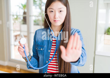 Schöne asiatische Frau prüfen health care mit Stethoskop mit offener Hand das STOP-Schild mit ernsten und selbstbewussten Ausdruck, Verteidigung Geste Stockfoto