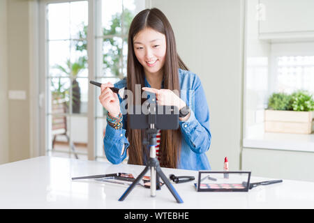 Schöne asiatische Einflussnehmer Frau Aufnahme Make-up Tutorial mit Smartphone Kamera sehr zufrieden zeigte mit Hand und Finger Stockfoto