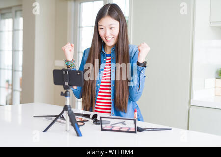 Schöne asiatische Einflussnehmer Frau Aufnahme Make-up Tutorial über Smartphone-kamera feiern überrascht und für den Erfolg mit erhobenen Armen erstaunt und Stockfoto
