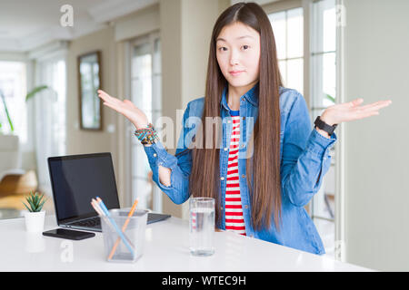Schöne asiatische Frau mit Computer Laptop ratlos und verwirrt Ausdruck mit den Armen und hob die Hand. Zweifel Konzept. Stockfoto