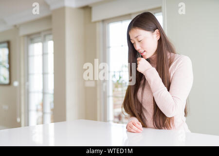 Schöne asiatische Frau legere Pullover am weißen Tisch Unwohlsein und als Symptom für kalte oder Bronchitis Husten. Healthcare Konzept. Stockfoto