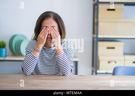 Mittleren Alters ältere Frau am Tisch zu Hause sitzen die Augen reiben für Ermüdung und Kopfschmerzen, schläfrig und müde Ausdruck. Vision Problem Stockfoto