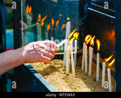 Woman's Hand Beleuchtung Kerze im Sockel der Kirche. Close-up schießen. Religion. Stockfoto