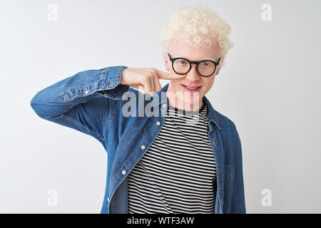 Junge albino blonder Mann tragen Jeanshemd und Gläser über isoliert weißer Hintergrund zeigt mit der Hand Finger zu Gesicht und Nase und lächelt freundlich. Werden Stockfoto