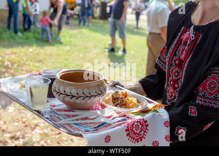 Frau in Schwarz nationalen Bluse bestickt mit roten und weißen Fäden Holding ein Fach mit besticktem Handtuch abgedeckt. Traditionelle ukrainische Lebensmittel borsch Stockfoto