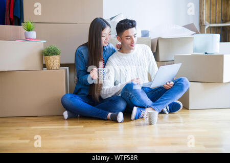 Jungen asiatischen Paar sitzen auf dem Boden des neuen Hauses rund um Kartons mit Laptop und einer Tasse Kaffee Stockfoto