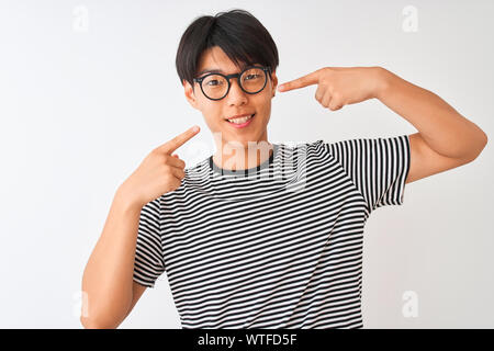 Chinesischer Mann mit Brille und Marine gestreiftes T-Shirt stehend über isoliert weißer Hintergrund lächelt Fröhlich angezeigt und zeigen mit den Fingern Zähne Stockfoto