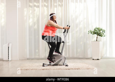 Übergewichtige Frau Training auf einem stationären Fahrrad zu Hause Stockfoto