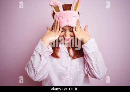 Junge schöne rothaarige Frau in Pyjama über rosa isoliert Hintergrund Kopfschmerzen leiden, verzweifelte und betonte, weil Schmerz und Migräne. Uhr Stockfoto