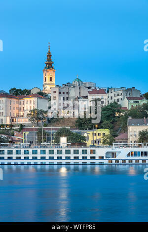 Blaue Stunde Blick auf Belgrad riverfront mit Fluss Sava im Vordergrund, heiligen Erzengel Michael Kathedrale an der Rückseite und beeindruckend und großen Cruiser Stockfoto