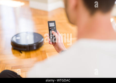 Nahaufnahme des Menschen Hände Steuerung automatische Staubsauger können Sie über die elektronische Steuerung der Roboter wischen Stockfoto