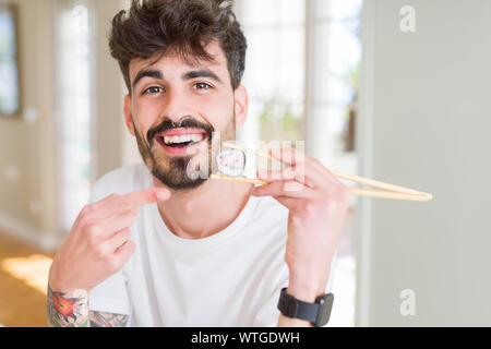 Junger Mann essen asiatische Sushi mit Stäbchen sehr glücklich zeigte mit Hand und Finger Stockfoto