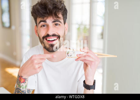 Junger Mann essen asiatische Sushi mit Stäbchen sehr glücklich zeigte mit Hand und Finger Stockfoto