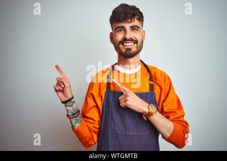 Junge Ladenbesitzer Mann mit Tattoo tragen Schürze stehend über isoliert weißer Hintergrund lächelt und schaut in die Kamera zeigte mit zwei Händen und f Stockfoto