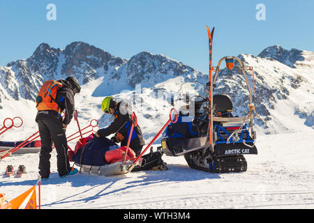 Pyrenäen, ANDORRA - Februar 13, 2019: Retter in einem Skigebiet bereiten Sie die Opfer für den Transport. Zwei Rettungskräfte legen die auf einem Schlitten ag verletzt Stockfoto