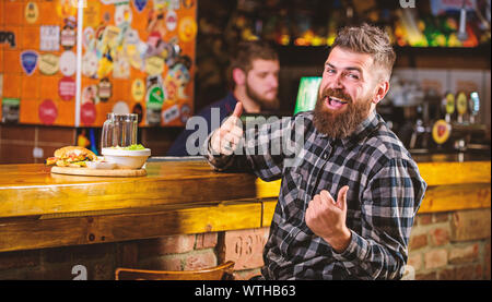 Essen im Pub. Kalorienreiche Snacks. Hipster entspannen im Pub. Pub ist ein entspannender Ort Drink zu entspannen. Brutale hipster bärtigen Mann an der Theke sitzen. Mann mit Bart Bier trinken essen burger Menü. Stockfoto