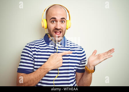 Junger Mann Musik tragen gelbe Kopfhörer über isolierte Hintergrund erstaunt und lächelt in die Kamera während der Präsentation mit Hand- und pointi Stockfoto