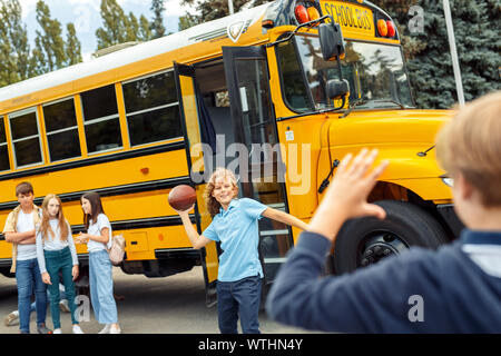 Mitschüler in der Nähe von Rugby School Bus spielen aufgeregt lächelnd Stockfoto