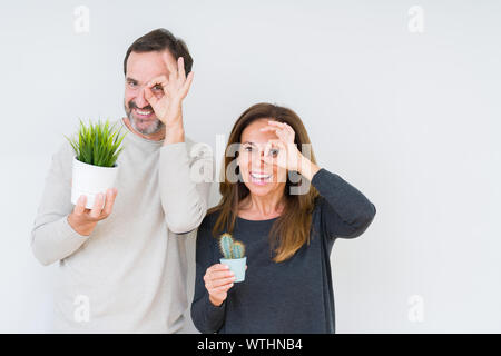 Mittleres Alter Paar hält Anlagen über isolierte Hintergrund mit glücklichen Gesicht lächelnd tun ok Zeichen mit der Hand auf Auge schauen durch die Finger Stockfoto