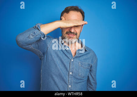 Stattliche mittleren Alters älterer Mann mit dem grauen Haar über isolierte blauen Hintergrund, die Augen mit der Hand und schaut ernst und traurig. Sightless, Verstecken und Re Stockfoto