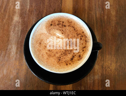 Flach, oben von einem Chai Latte in einem schwarzen Schale auf Untertasse auf dunklen Holzmöbeln serviert betonte cafe Tabelle. Beliebte Kaffee trinken. Stockfoto