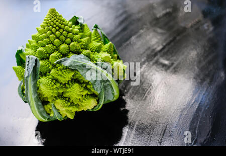 Erstaunliche frische grüne Romanesco Brokkoli oder römischen Blumenkohl auf nassem dunklen Hintergrund. Seine Form ist eine natürliche Annäherung an ein Fraktal. Nahaufnahme. Stockfoto