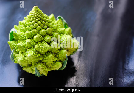 Erstaunliche frische grüne Romanesco Brokkoli oder römischen Blumenkohl auf nassem dunklen Hintergrund. Seine Form ist eine natürliche Annäherung an ein Fraktal. Nahaufnahme. Stockfoto