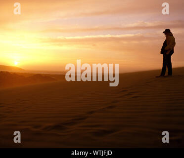 Mann stand auf Sand dune den Sonnenuntergang zu beobachten. Stockfoto