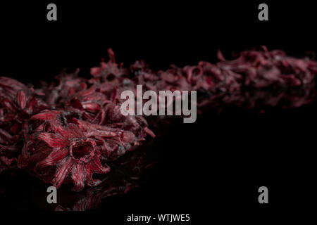 Menge ganz süßen roten kandierten Hibiscus diagonal auf schwarzem Glas isoliert Stockfoto