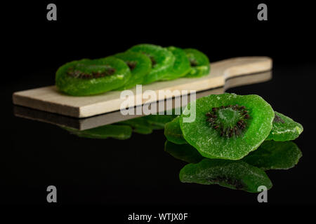 Gruppe der acht Scheiben süß grün kandierte Kiwis auf kleinen hölzernen Schneidebrett auf schwarzem Glas isoliert Stockfoto