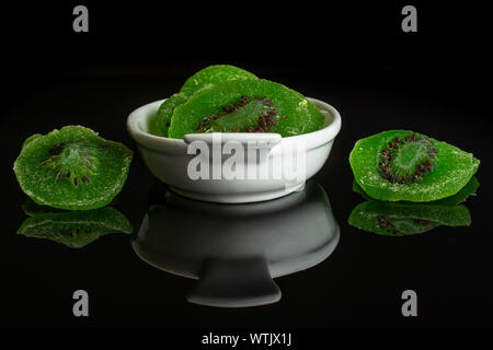 Viele Scheiben süß grün kandierte Kiwis in weiße, ovale Keramik Schüssel auf schwarzem Glas isoliert Stockfoto