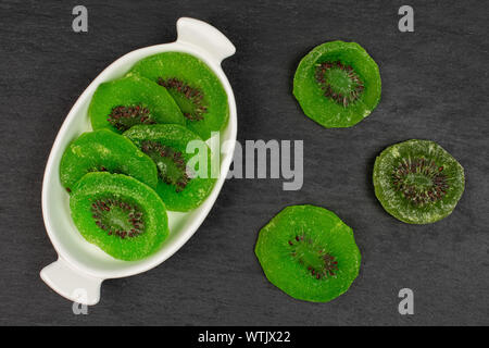 Gruppe der acht Scheiben süß grün kandierte Kiwis in weiße, ovale Keramik Schüssel flatlay am grauen Stein Stockfoto