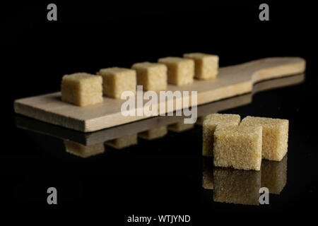 Gruppe der Acht ganze süßen braunen Zucker Würfel auf kleinen hölzernen Schneidebrett auf schwarzem Glas isoliert Stockfoto