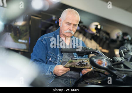 Mann sitzt auf Motorrad und Broschüre Stockfoto