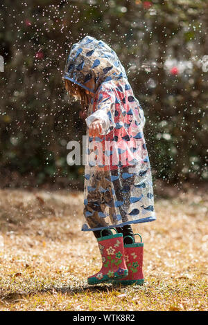 Kleines Mädchen in Regenmantel und Stiefel wandern im Regen Stockfoto