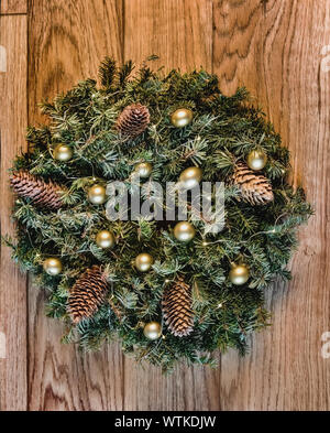 Weihnachten und neues Jahr eingerichtet. Ein Kranz aus Zweigen mit Zapfen Ornament, Lichter von einer Girlande und goldenen Kugeln. Traditionelle Weihnachten Dekoration für i Stockfoto