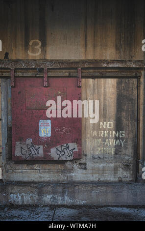 Eine geschlossene rote Tür an der Außenseite eines alten Industriegebäudes mit der Aufschrift „No Parking Tow Away Zone“ Stockfoto