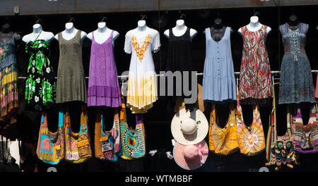 Farbenfrohe Ausstellung von Sommerkleidern, Stofftaschen und Hüten auf Schaufensterpuppen und Regalen an einem Verkaufsstand im Freien Stockfoto