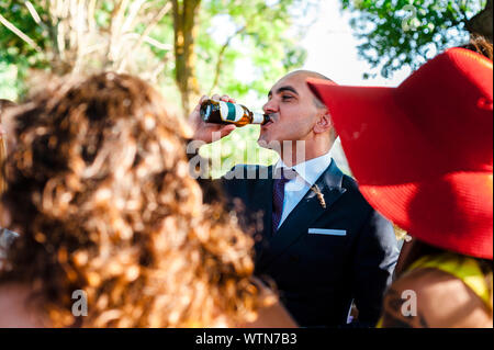 Durstig Bräutigam Bier trinken die Gäste umgeben nach Hochzeit celeb Stockfoto