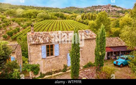 Hohe Betrachtungswinkel von einer Straße von einem traditionellen alten Bauernhof aus Stein Haus und malerischen Traube Weinberg, mit symmetrischen Reihen von Reben in der Provence, Frankreich. Stockfoto