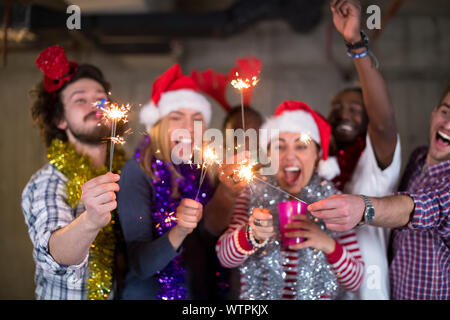 Multiethnische Gruppe junger happy and Business Leute Beleuchtung eine Wunderkerze und Spaß beim Silvester feiern in der betonwand an Stockfoto
