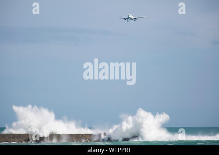 Ein Flugzeug fliegt Air New Zealand als dünung stürzt in eine breakwall bei Lyall Bay, Wellington, Neuseeland. Stockfoto