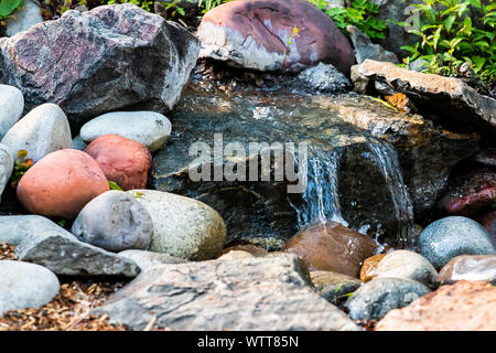 Kleine Springbrunnen Wasserfall closeup in Garten Park mit Teich und bunte Steine in Colorado Stockfoto