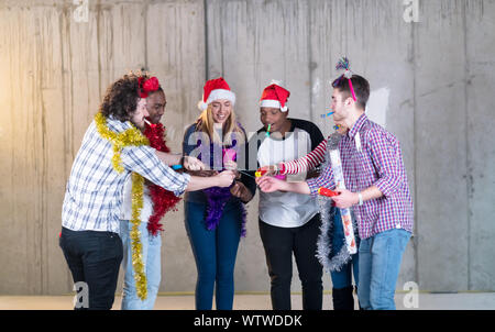 Multiethnische Gruppe junger happy and Business Leute Beleuchtung eine Wunderkerze und Spaß beim Silvester feiern in der betonwand an Stockfoto