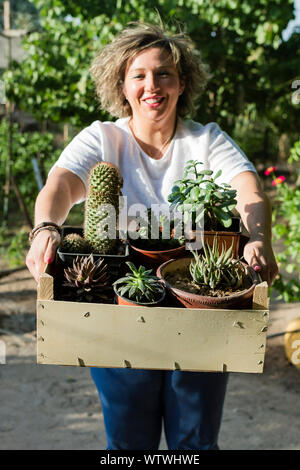 Junge Frau lächelt, als sie zeigt ihre captus und Pflanzen auf einem sonnigen d Stockfoto