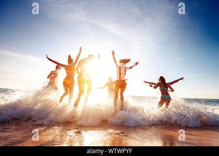 Große Gruppe von Sieben glückliche Freunde ist Spaß und läuft bei Sonnenuntergang Strand Sonne Licht und Wellen Stockfoto