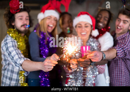 Multiethnische Gruppe junger happy and Business Leute Beleuchtung eine Wunderkerze und Spaß beim Silvester feiern in der betonwand an Stockfoto