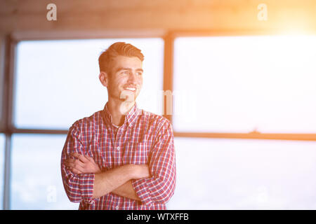 Porträt der jungen casual Geschäftsmann stand mit verschränkten Armen auf der Baustelle und Sonnenlicht durch die Fenster beim Verschieben in neuen Anlauf Stockfoto