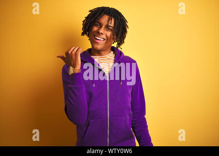 Afro-amerikanische Mann mit Dreadlocks tragen lila Sweatshirt über isolierte lila Hintergrund lächelnd mit glücklichen Gesicht schauen und zeigen auf der Seite w Stockfoto